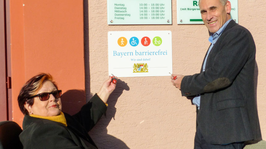 Waltraud Joa und Dr. Wolfgang Hell bringen das Signet „Bayern barrierefrei“ am Rathaus an.