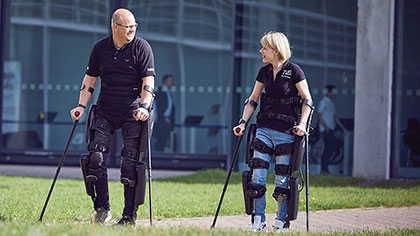 Ein Mann und eine Frau gehen mit ihren Exoskeletten und Krücken spazieren.