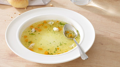 Nahaufnahme: Suppenteller mit Brühe und Löffel.