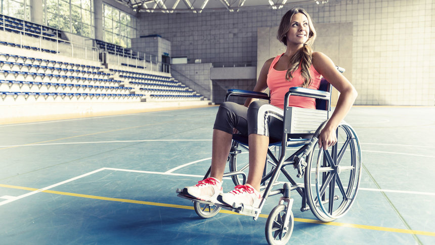Junge Rollstuhlfahrerin in einer Sporthalle. Sie trägt Sportkleidung.