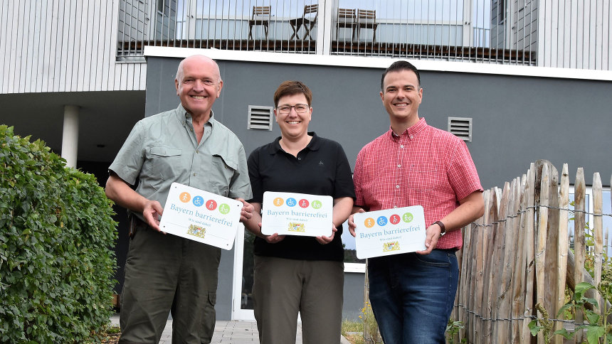 Gruppenbild: Präsentation des Signets „Bayern barrierefrei“ vor einem Gebäude. 