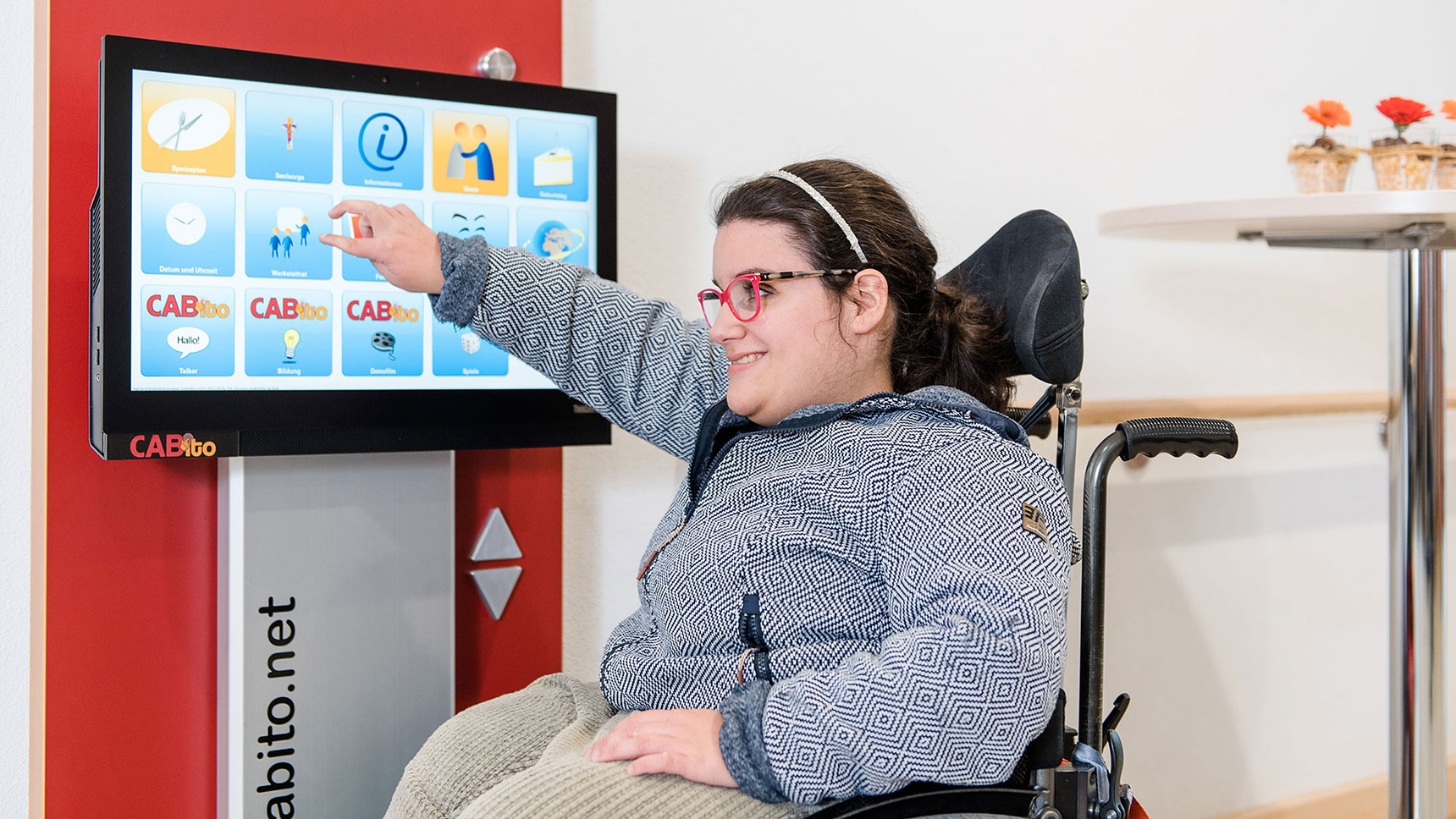 Junge Frau im Rollstuhl bedient Info-Terminal mit Touch-Display.