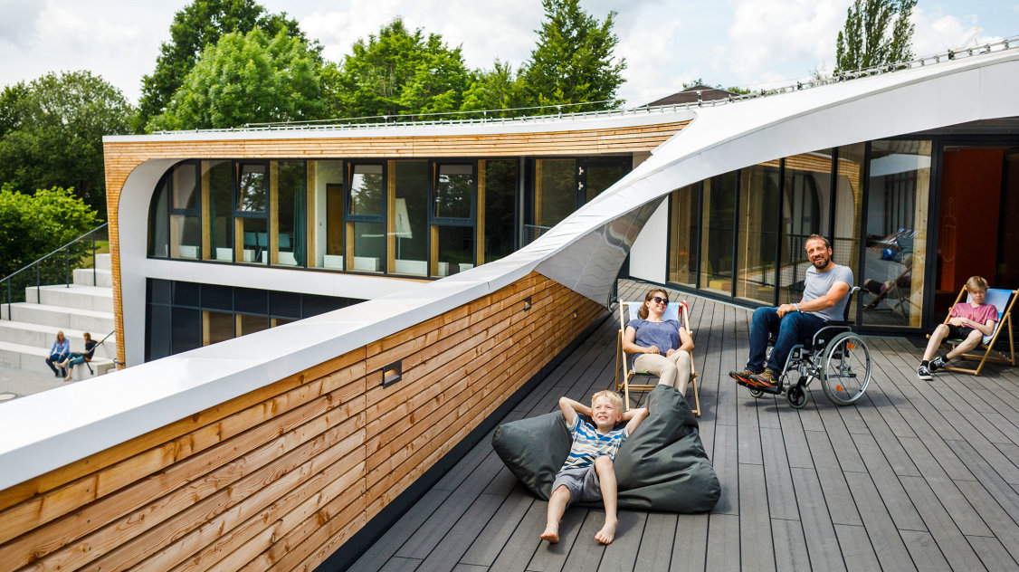 Eine Familie auf einer großen Terrasse. Der Vater sitzt im Rollstuhl.