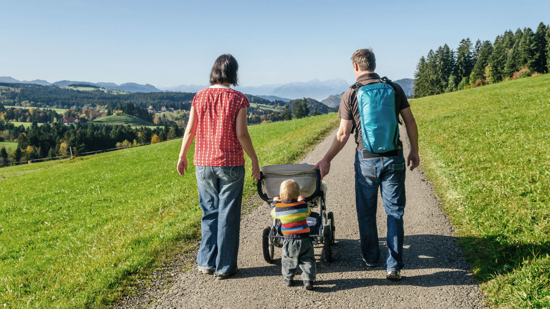 Familie mit Kinderwagen auf einem Spazierweg im Grünen.