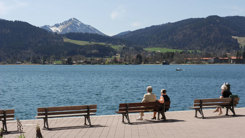 Am See: Zwei ältere Menschen sitzen auf einem Steg auf einer Bank.