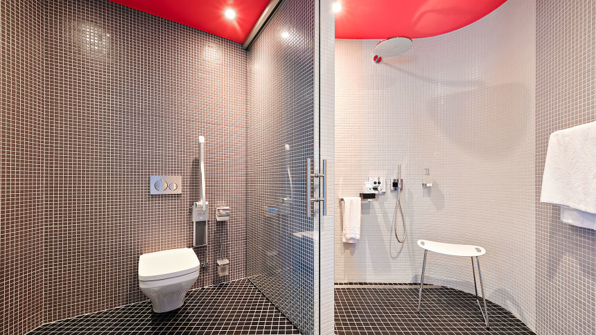 Ein barrierearmes Bad mit WC und Dusche ist in neutral-weißes Licht getaucht.