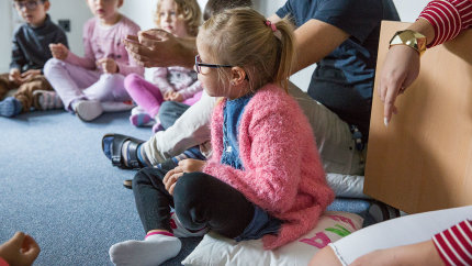 Lena und andere Kinder sitzen im Kreis bei einem Spiel.