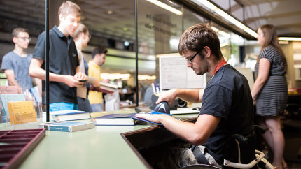 Studierende an der Bücherausleihe. Leonard Zenke scannt Bücher ein.