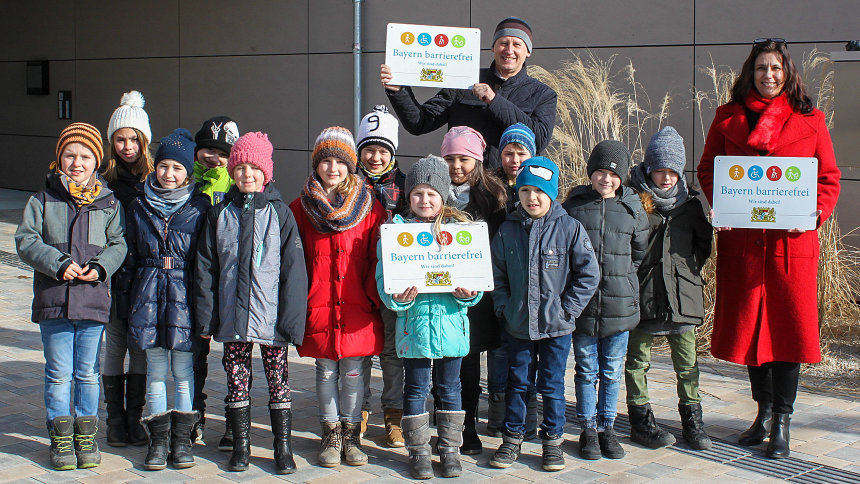 Gruppenbild: Kinder und Erwachsene zeigen Signets „Bayern barrierefrei“.