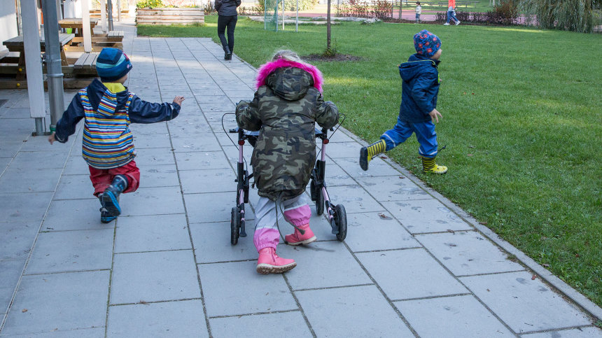 Lena läuft mit ihrem Rollator im Kita-Garten, zwei andere Kinder rennen neben ihr her.