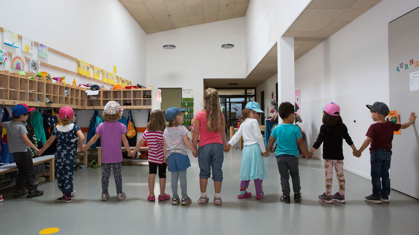 Mehrere Kita-Kinder stehen Hand in Hand nebeneinander über die gesamte Breite des Flures.