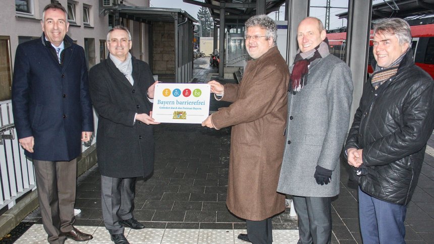 Gruppenbild: Übergabe des Signets „Bayern barrierefrei“ auf einem Bahnsteig.