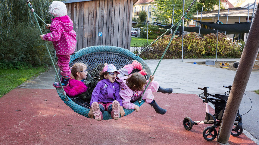 Lena und weitere Kinder in einer Nestschaukel; Lenas Rollator steht daneben.