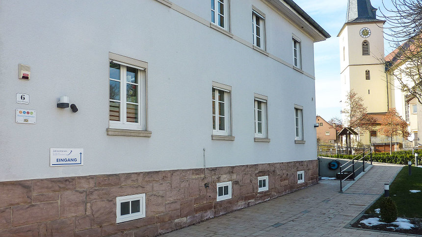 Gebäude mit Zugangsrampe, an der Hauswand das Signet „Bayern barrierefrei“.