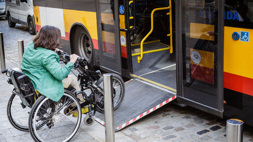 Frau im Rollstuhl fährt über eine ausklappbare Rampe in einen Linienbus.