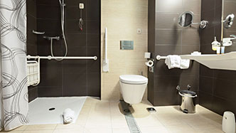 Ein Badezimmer mit barrierefreier Dusche, WC mit klappbarem Haltegriff und unterfahrbarem Waschbecken.