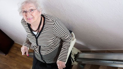 Ältere Frau mit Brille sitzt im Treppenlift.