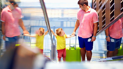 Mann und Kind fahren mit Koffer eine Rolltreppe hoch.