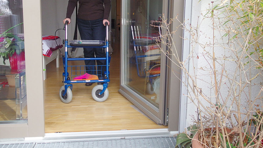 Karin K. steuert mit dem Rollator aus der Wohnung auf den Balkon zu.