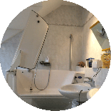 Badezimmer mit Dusch-WC, absenkbarem Waschbecken, kippbarem Spiegel und einer Badewanne mit Tür