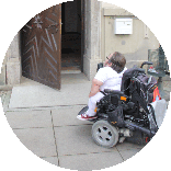 Benedikt Lika mit seinem Rollstuhl vor der geöffneten Tür eines historischen Gebäudes. Über der Tür steht die Aufschrift „Ratskeller“.