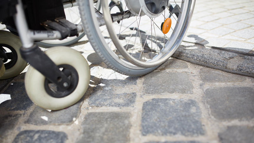 Nahaufnahme: Rollstuhlreifen an abgesenkter Bordsteinkante.