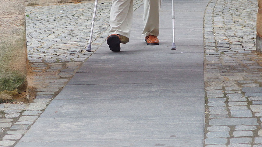 Mann mit Krücken auf Gehweg mit unterschiedlichen Belägen.