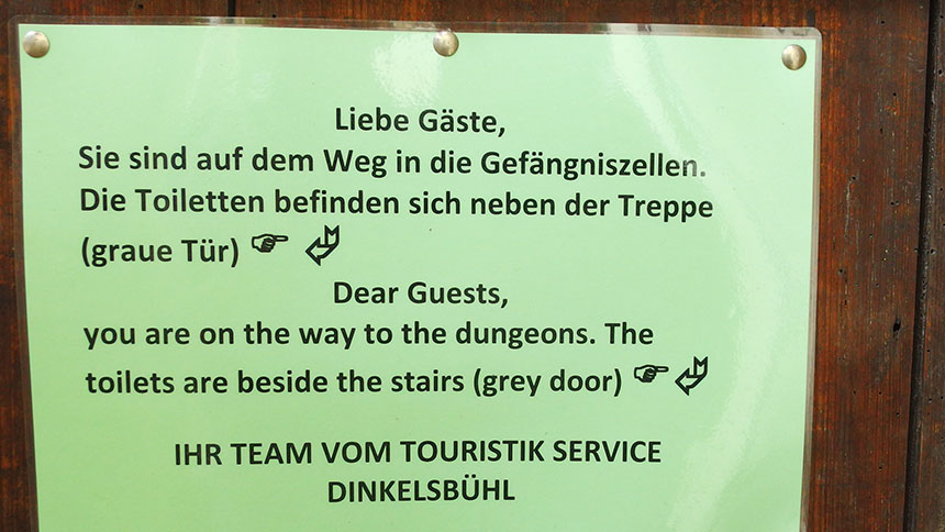 Hinweisschild: „Liebe Gäste, Sie sind auf dem Weg in die Gefängniszellen. Die Toiletten befinden sich neben der Treppe.“