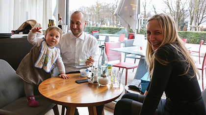 Junge Familie am Lounge-Tisch (zwei Bilder); der Vater füttert seine kleine Tochter.