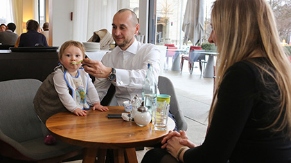 Junge Familie am Lounge-Tisch (zwei Bilder); der Vater füttert seine kleine Tochter.