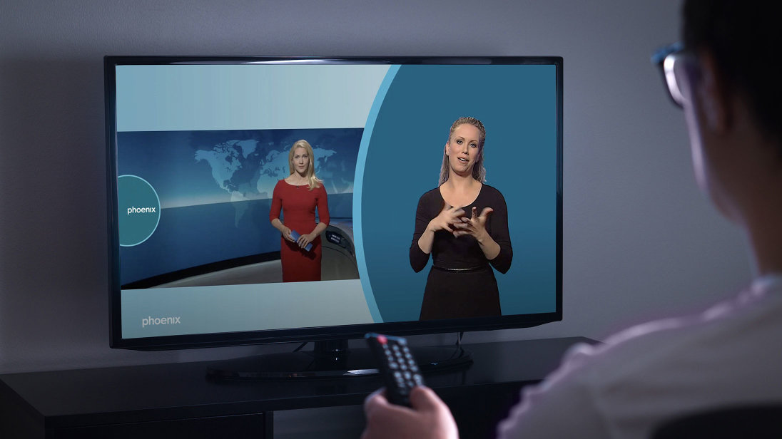 Ein Bildschirm zeigt eine Szene einer Nachrichtensendung mit zusätzlicher Gebärdensprachdolmetscherin.   