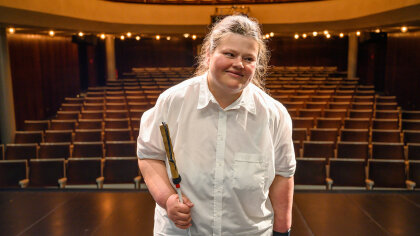 Porträtfoto: Yvonne Burkhardt steht allein auf einer Theaterbühne, hinter ihr der leere Zuschauerraum.