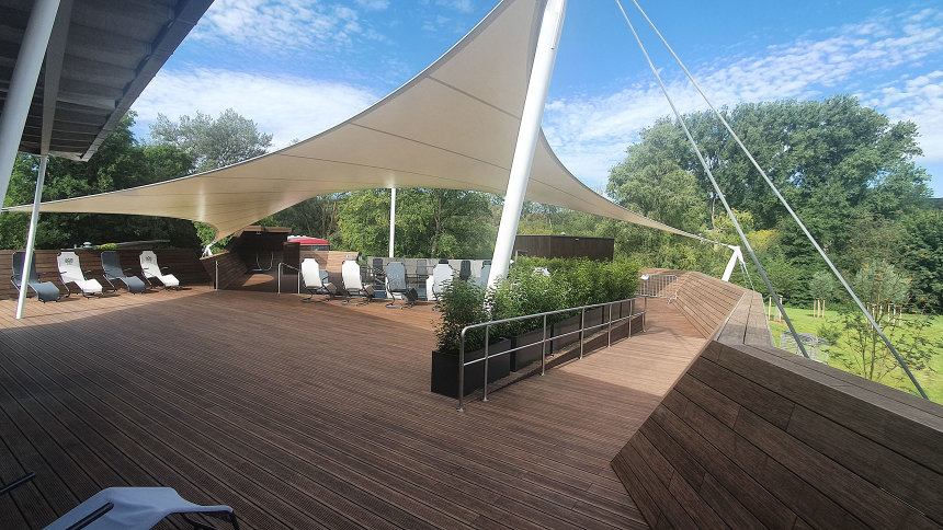 Eine große Terrasse mit Holzboden, teilweise von einem Sonnensegel überspannt.