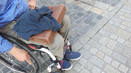 Florian Stangl steht mit seinem Rollstuhl in einer Fußgängerzone, am Übergang von grober zu abgeflachter, rollstuhlfreundlicher Pflasterung. 