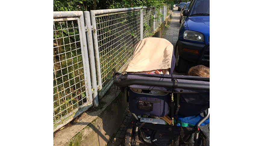 Ein Doppelkinderwagen steht auf einem Bürgersteig. Ein parkendes Auto versperrt den Weg.