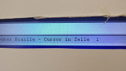 Ein Computer-Bildschirm ist bis auf eine Anzeigezeile mit einer Papphülle abgedeckt. Der Text in der Zeile lautet: „Cursor in Zelle 1“.