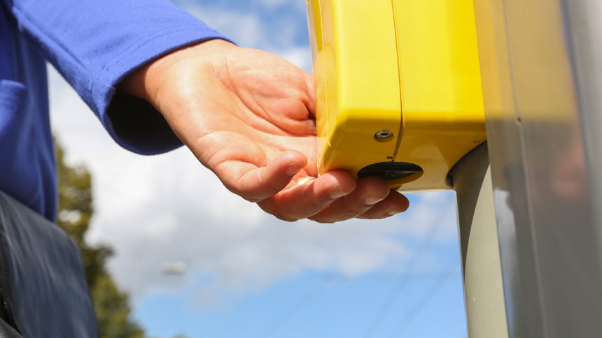 Nahaufnahme einer Blindenampel von unten. Eine Hand liegt auf der Pfeiltaste.