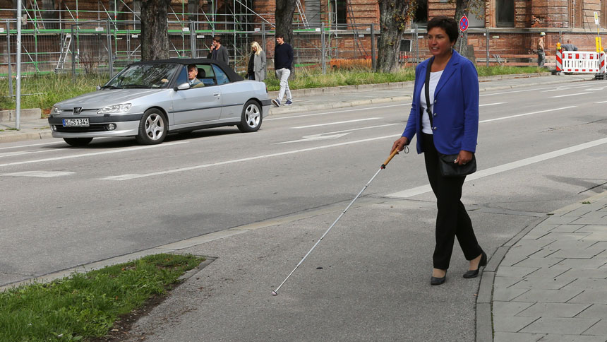 Irmgard Badura tritt vom Gehweg auf eine Fahrradspur. Fuß- und Radweg sind sichtbar, aber nicht taktil erfassbar voneinander abgesetzt.