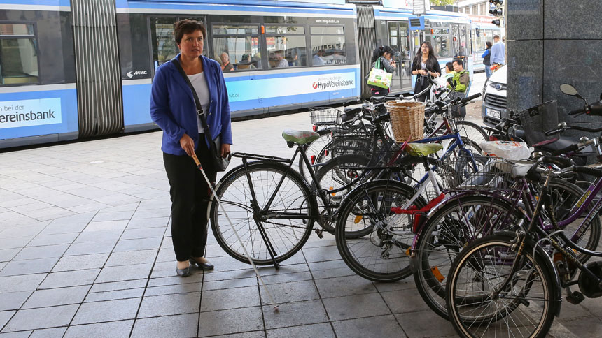 Irmgard Badura läuft an einer Reihe geparkter Fahrräder vorbei. Dabei streift sie ein Fahrrad, das aus der Reihe hervorragt.