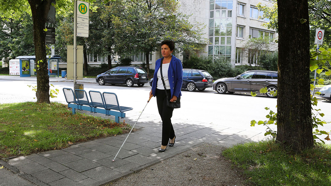 Irmgard Badura ist mit dem Langstock unterwegs an der Münchner Bushaltestelle Infanteriestraße.