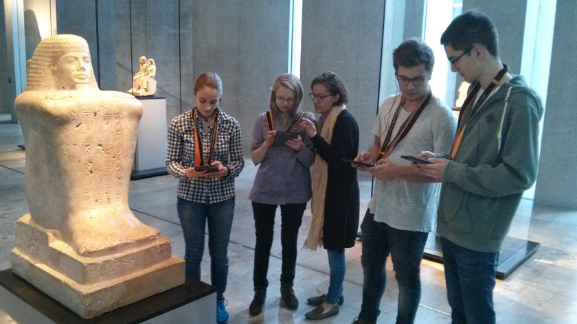 Gruppe von Jugendlichen mit Multimedia-Guides vor einer Skulptur.