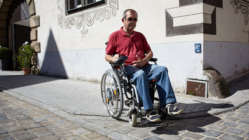 Wolfram Arnold fährt mit dem Rollstuhl über einen abgesenkten Bordstein.