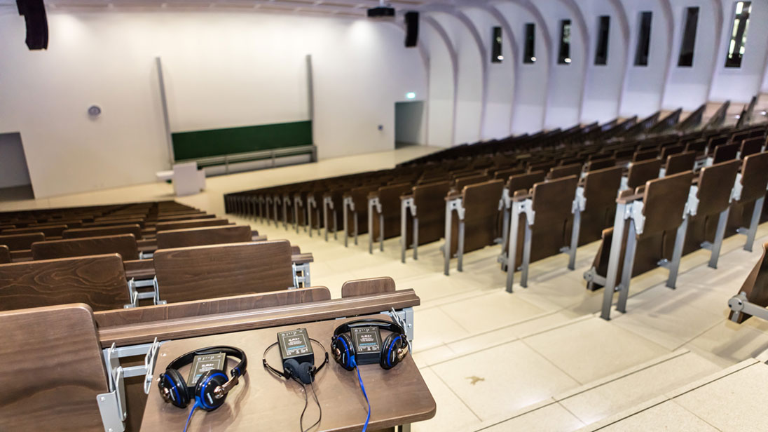 Großer Hörsaal; im Vordergrund Ablage mit Audio-Empfangsgeräten.