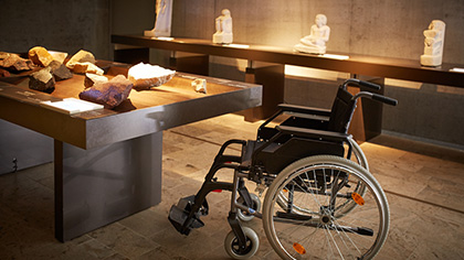 (Leerer) Rollstuhl vor einem Präsentationstisch mit Gesteinsproben.