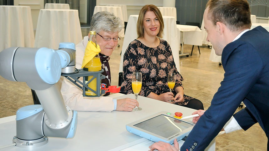 Computergesteuerter Roboterarm serviert zwei Testerinnen Orangensaft.