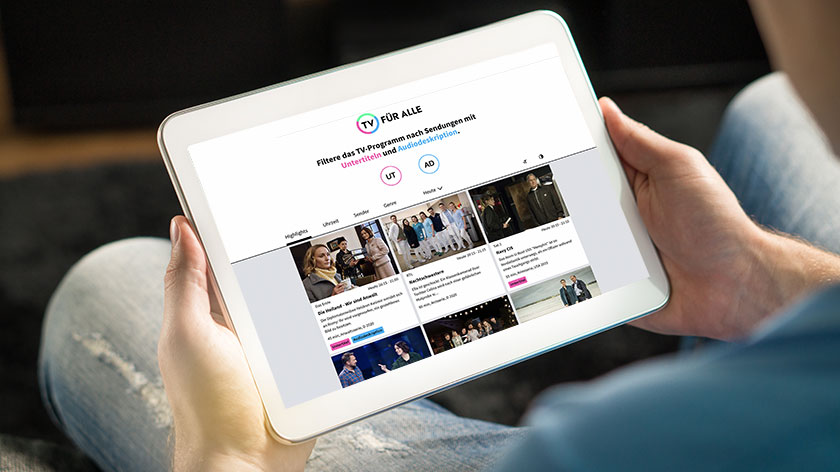 Nahaufnahme: Eine Person hält ein Tablet in den Händen. Es zeigt eine Website mit TV-Programm.