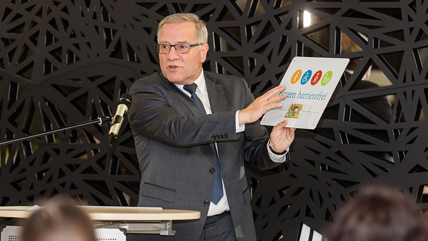 Johannes Hintersberger mit dem Signet „Bayern barrierefrei“ am Rednerpult der LMU.