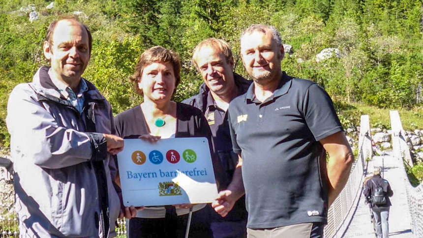 Gruppenbild: Übergabe des Signets „Bayern barrierefrei“ auf einer hölzernen Hängebrücke.