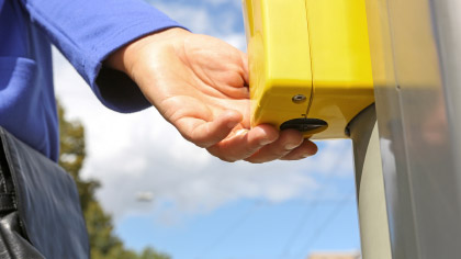 Eine Person drückt mit den Fingern auf die Signaltaste einer Blindenampel.