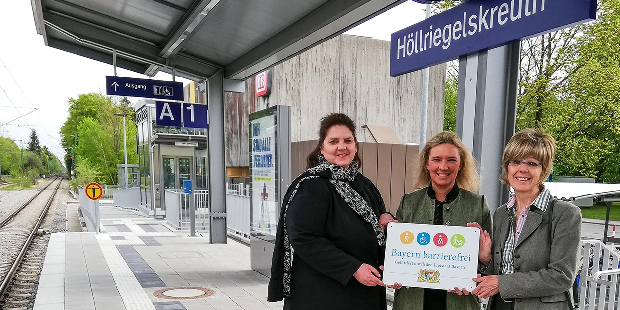Gruppenbild: Übergabe des Signets „Bayern barrierefrei“ auf einem Bahnsteig.